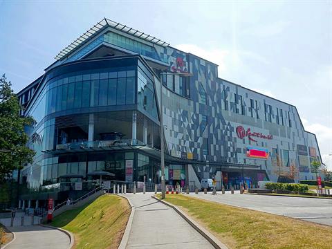 The glazed corner of the Resorts World Birmingham complex on a bright day, with a terrace on the lower floor and a pavement leading to the entrance.